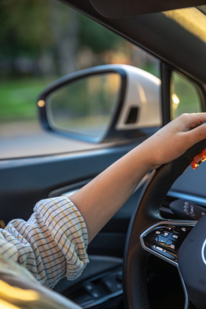 Young woman driving a car. Hands on the wheel. Side mirror in the car.